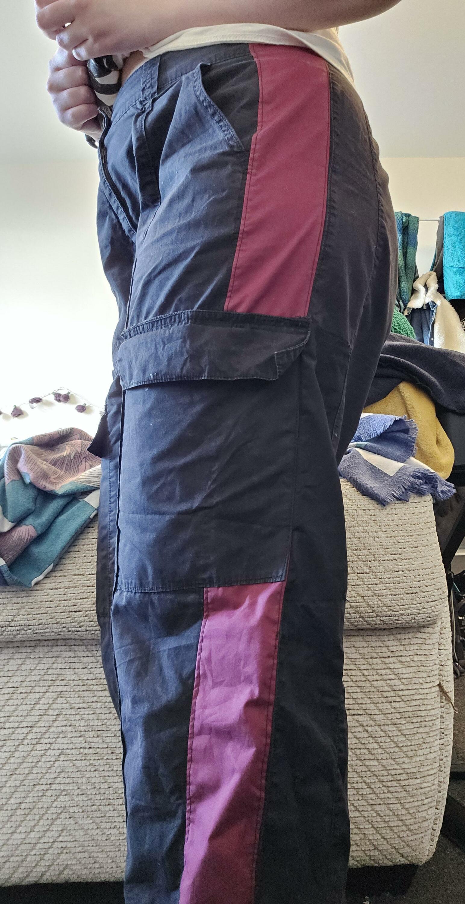 A person standing in side profile. They are wearing a pair of black cargo pants, showing the stripe of red fabric running down the side seam.